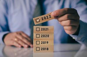 A business man is choosing the 2022 option to celebrate the approaching new year. with wooden blocks and year icons photo