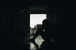 un joven agotado por los problemas de la vida. con un sentimiento de depresión y estrés sentado en un pasillo oscuro concepto de vida malo e infeliz foto