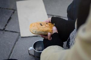 A homeless beggar eating bread and asking for help from passersby. photo