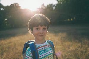 un niño con una mochila camina en el prado foto