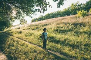 un niño con una mochila camina en el prado foto