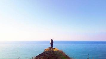 Male Person stands on edge of the cliff looking around confused with panoramic view of vast sea in background video