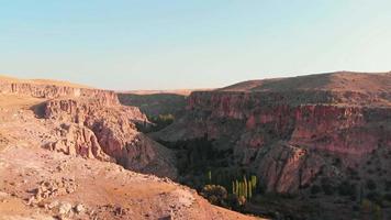 zoom arrière sur les falaises rocheuses pittoresques de la vallée d'ihlara avec de belles textures au coucher du soleil avec la vallée des arbres verts video
