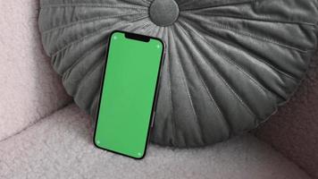 Smartphone moderno con pantalla verde chromakey en la acogedora silla acostada sobre una elegante almohada closeup