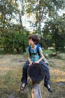 A boy with a backpack sits on the trunk of a fallen tree photo