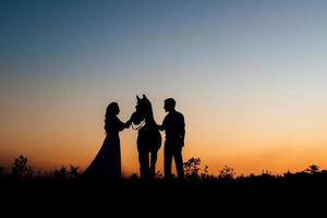 Silhouettes of a bride in a white dress and a groom in a white shirt on a walk photo