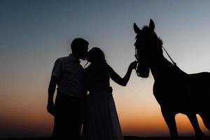 Silhouettes of a bride in a white dress and a groom in a white shirt on a walk photo