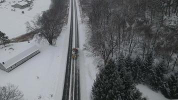 Snow plow cleaning highway in midwest Wisconsin. Mountainside with bare trees and evergreens. Small neighborhood seen in valley. video