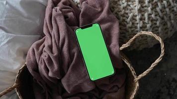 Modern smartphone laying on cozy grey blanket at home with green screen chromakey video