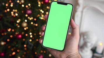 man håller smartphone med grön skärm chromakey över julgran med ljus video