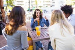 Grupo multiétnico de amigos tomando una copa juntos en un bar al aire libre.