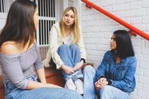 Multi-ethnic group of three friends sitting on street steps talking. photo