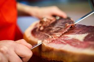 Professional cutter carving slices from a whole bone-in serrano ham photo