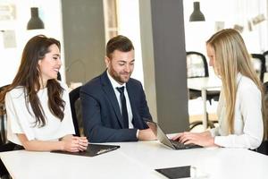 Blonde businesswoman explaining with laptop to smiling young couple. photo