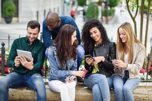 Jóvenes multiétnicos que utilizan teléfonos inteligentes y tabletas al aire libre foto