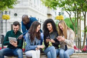 Jóvenes multiétnicos que utilizan teléfonos inteligentes y tabletas al aire libre foto