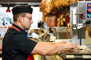 Male butcher cutting ham bones in a cutting machine photo