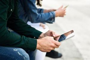 Jóvenes irreconocibles que usan teléfonos inteligentes y tabletas al aire libre foto