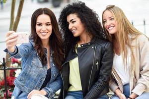 Multi-ethnic young women taking a selfie photograph together outdoors photo