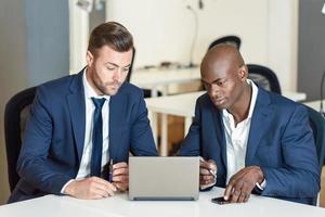 Empresarios negros y caucásicos mirando una computadora portátil foto