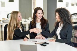 Three businesswomen shaking hands in a modern office