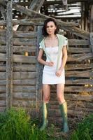 Asian woman, posing near a tobacco drying shed, wearing a white dress and green wellies.