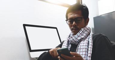 An Asian man uses a phone while working on a desk with a computer. photo