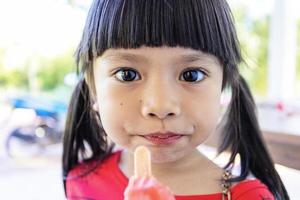 una niña asiática está comiendo felizmente helado. foto