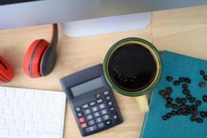 The work desk has a coffee cup and red headphones and office supplies. photo