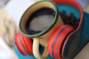 The work desk has a coffee cup and red headphones and office supplies. photo