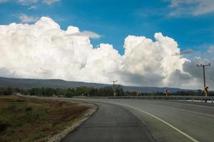 An empty road leading to large mountains with large clouds and sky photo