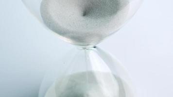 Close up, White sand in clear glass. Time running out when the sand flows down. On the white background.
