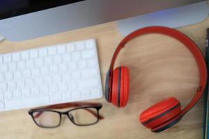 The work desk has a coffee cup and red headphones and office supplies. photo