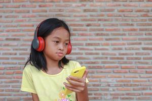 una linda chica asiática usa un auricular inalámbrico rojo para escuchar música en su teléfono foto