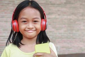 una linda chica asiática usa un auricular inalámbrico rojo para escuchar música en su teléfono foto