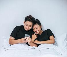 dos mujeres amorosas durmiendo y jugando teléfonos inteligentes. foto