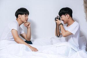 Two beloved young men sat on the bed and took pictures by the camera. photo