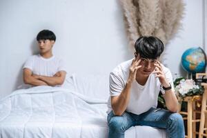 Two young men were angry on the bed and the other sat at the edge of the bed and was stressed. photo