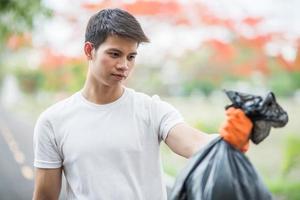 A man wearing orange gloves collecting garbage in a black bag.