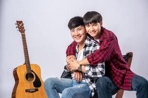 Two dear young men were sitting, cuddling in a chair, and with a guitar beside. photo