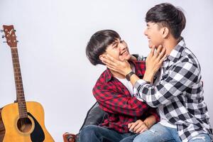 Two loving young men sitting on catch cheek On a chair and with a guitar by the side photo