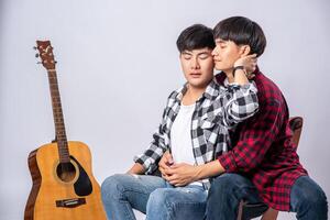 Two dear young men were sitting, cuddling in a chair, and with a guitar beside. photo