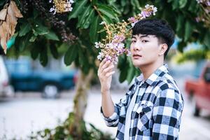 A young man in a striped shirt was standing on the roadside and holding the flower. photo