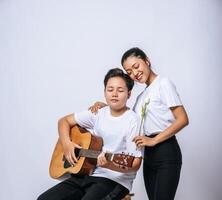 Two young women sat on a chair and played guitar. photo