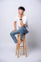 A young man in a white T-shirt is sitting on a high chair. photo