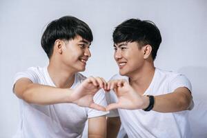 Two loving young men look at each other and make a hand of love symbol. photo