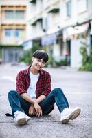 un joven con una camisa a rayas sentado en la calle foto