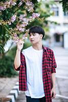 A young man in a striped shirt was standing on the roadside and holding the flower. photo