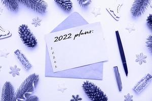 Top view of 2022 goals on sheet of paper and pen with envelope on table with winter decor toned very peri color photo