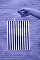 Close-up mock-up of eco-packaging on a brick very peribackground. Kraft bag in black and white stripes in a woman's hand. shopping photo